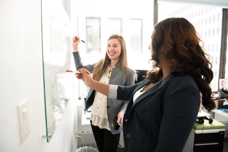 Photo of two people writing on a white board.